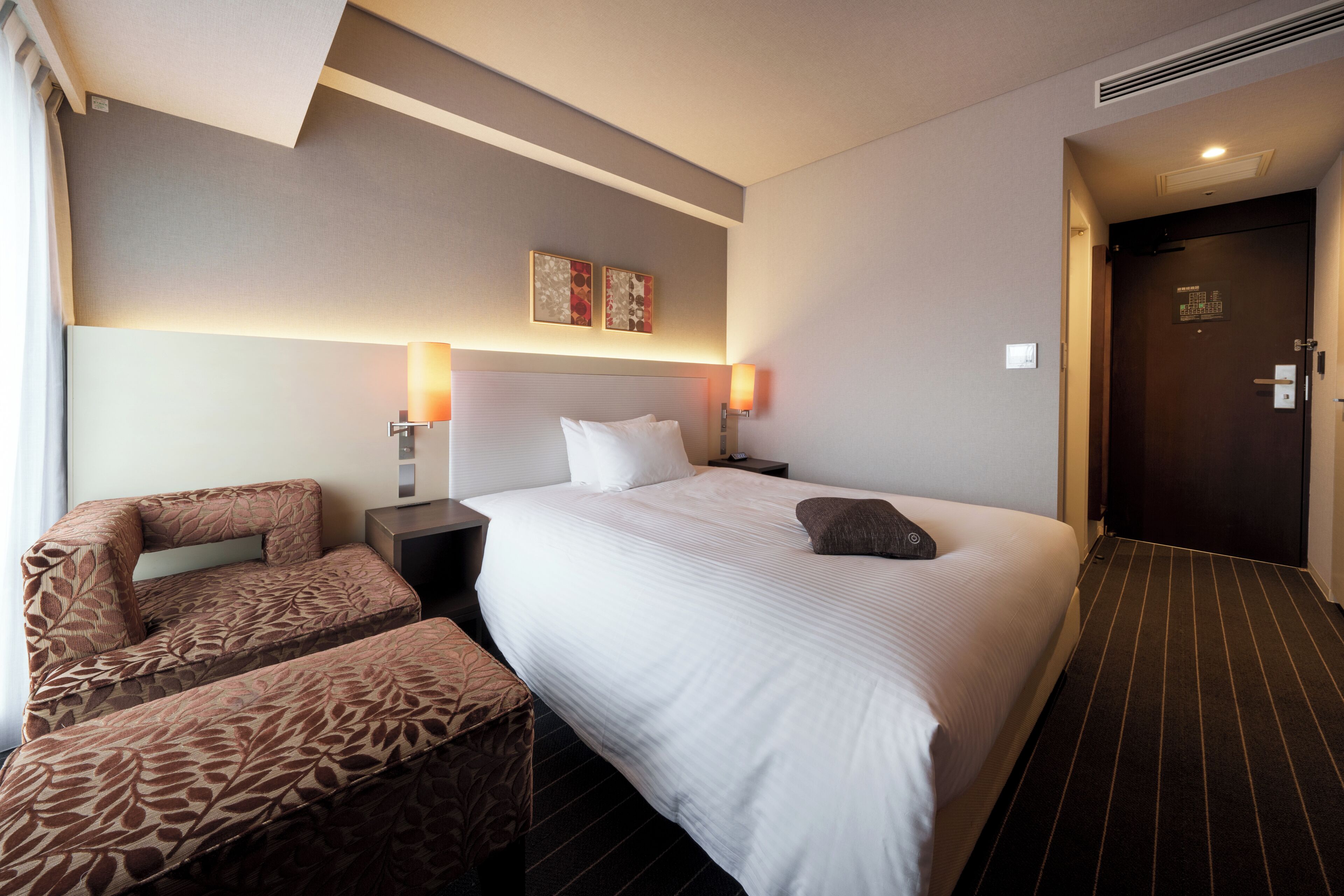A hotel room with a large bed, two bedside tables, a chair, and a door.