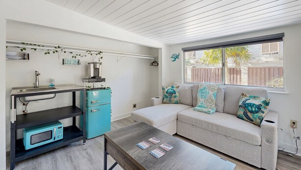 Un espacio habitable compacto con kitchenette, un sofá con cojines estampados y una ventana con vistas.