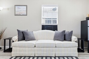 Ein Wohnzimmer mit einer Couch, einem gerahmten Bild an der Wand und einem Fenster mit Jalousien.