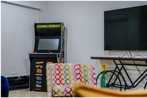 A room with a gaming console, a colorful sofa, a bicycle, and a TV. - Sunset Place (Homestead)
