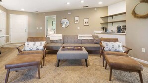 A living room with a sofa, two armchairs, and a coffee table. There is a kitchen area with a refrigerator and coffee maker.