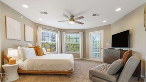 A bedroom with a bed, a chair, a television, and a ceiling fan.