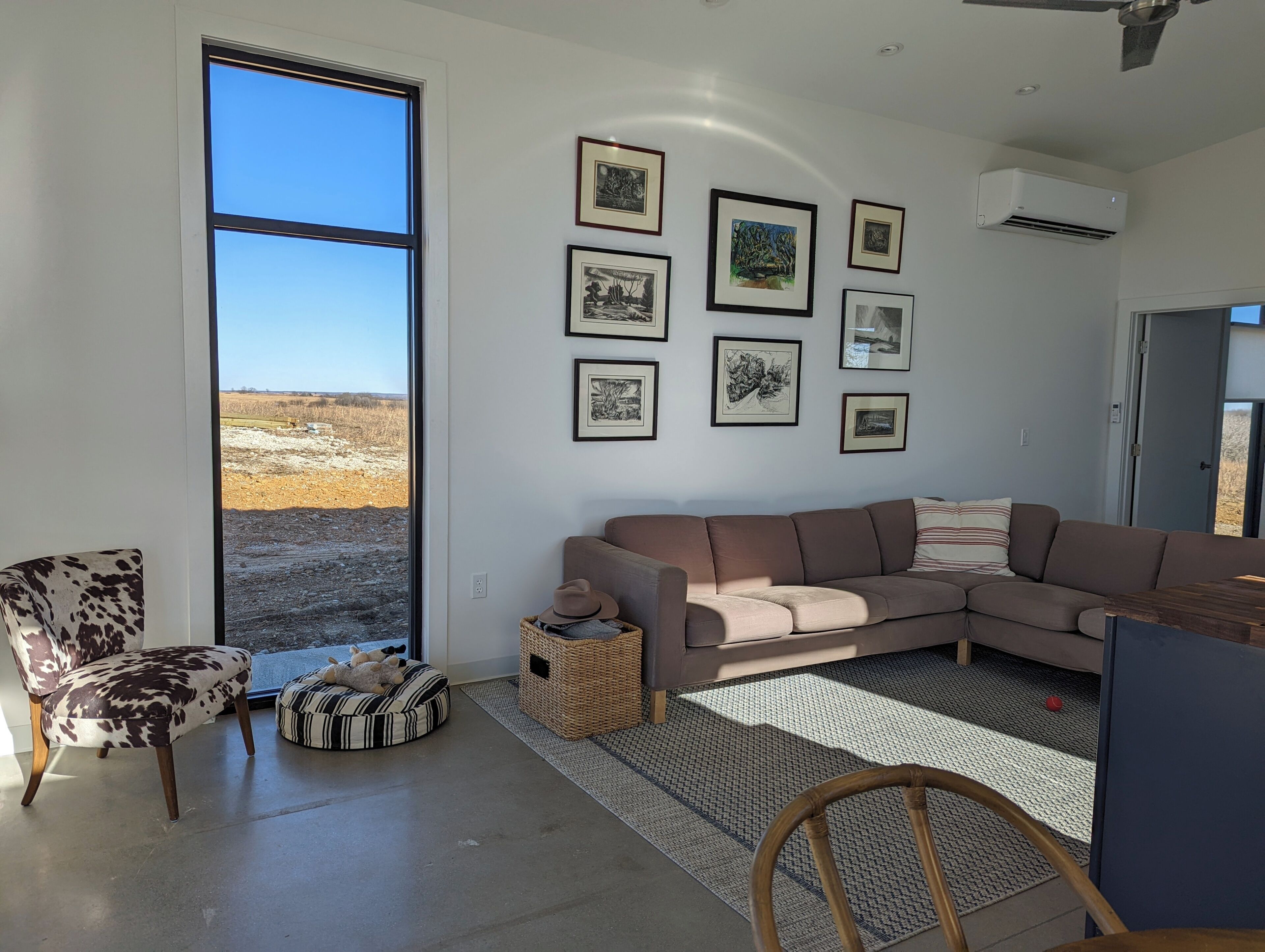 A modern living room with a large window, a sofa, a chair, and a wall adorned with framed artwork.