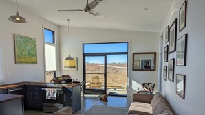 Ein modernes Wohnzimmer mit einer Couch, einem Essbereich mit Tisch und einem großen Fenster mit Blick auf eine Landschaft.