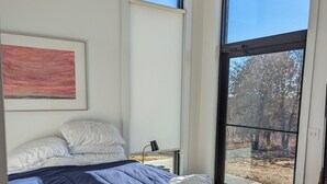 Ein Schlafzimmer mit einem Bett, einem gerahmten Gemälde und großen Fenstern.