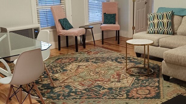 Un salon avec un ventilateur de plafond, deux fauteuils, un canapé, une table basse et un tapis à motifs.