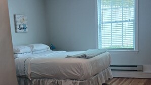 Une chambre à coucher comprenant un lit, un plancher en bois, un ventilateur de plafond, une fenêtre avec des stores et un élément de décoration murale.