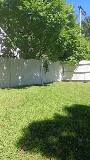 A grassy backyard with a white fence and trees.