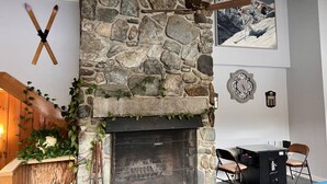 Una chimenea de piedra con repisa de madera, una decoración de pared con temática de esquí y un cuadro enmarco de un paisaje montañoso.