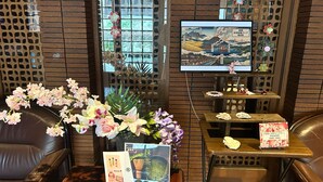A traditional Japanese room with tatami flooring, a low table with a vase of flowers, a television displaying a landscape, and a sign with Japanese text. - Kozuka Hisanoha (Hakone)