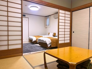 A traditional Japanese-style room with tatami flooring, a low wooden table, and a bed with a white and brown bedding. - Kozuka Hisanoha (Hakone)