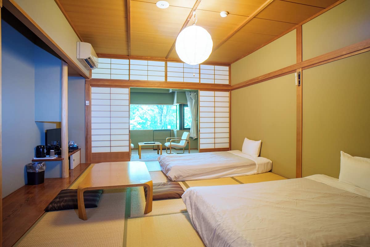 Una habitación tradicional japonesa con suelo de tatami, dos camas, un escritorio y vistas a zonas verdes.