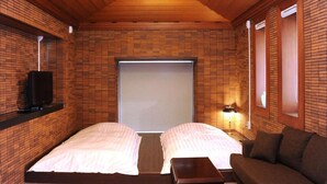 A room with a wooden ceiling, brick walls, a bed, a sofa, a TV, and a window. - Kozuka Hisanoha (Hakone)