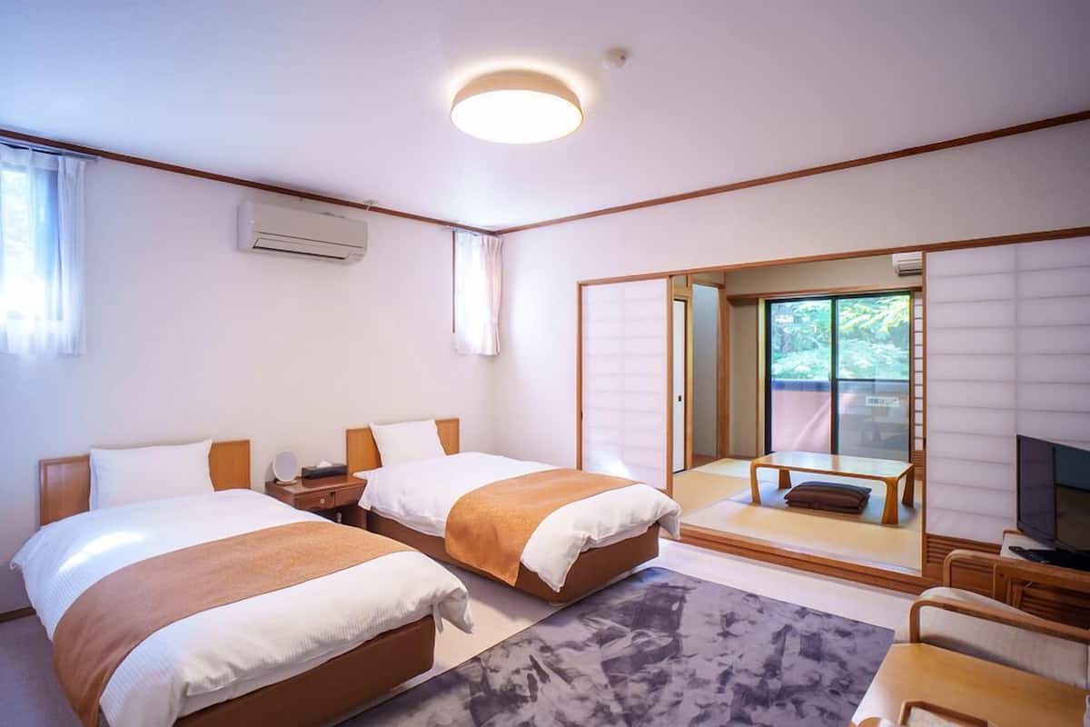 Habitación de hotel con dos camas, un sofá, un televisor y puerta corrediza a un balcón.