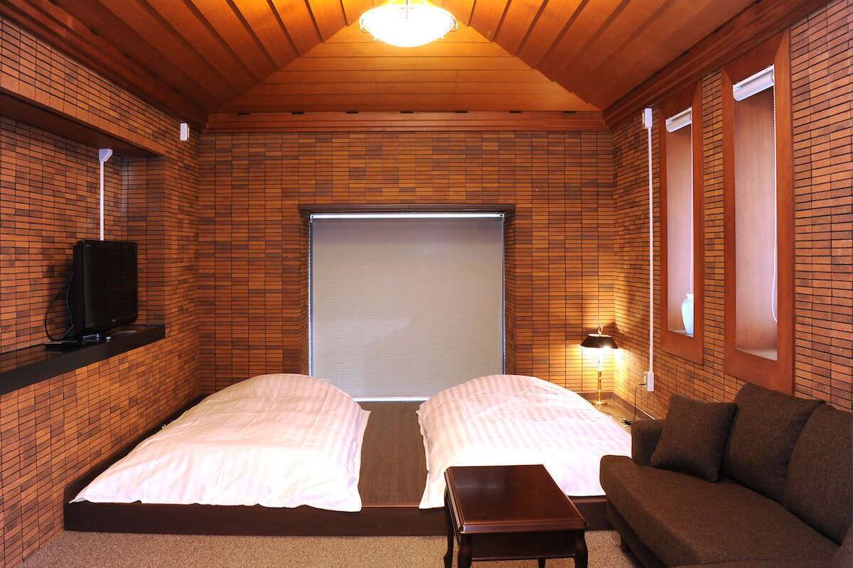 Una habitación con una cama, un sofá, un televisor en un estante, una ventana con persianas y una lámpara en el techo.