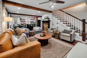 A spacious living room with a large brown leather sofa, a round coffee table, and a staircase with wooden railings.