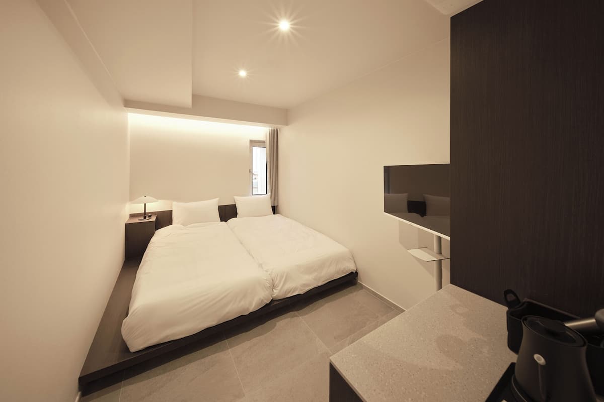 Une chambre d’hôtel moderne équipée d’un lit, d’une table de chevet, d’une lampe et d’une machine à café.