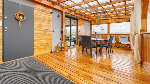 Un interior de madera con un ventilador de techo, un comedor con sillas y una mesa, y una vista a través de un ventanal.