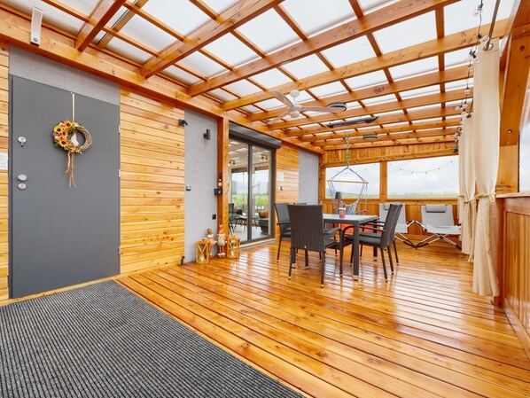 A wooden interior with a ceiling fan, a dining area with chairs and a table, and a view through a glass door.