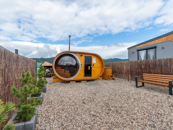 Una sauna de madera con un amplio ventanal circular, un banco y una valla de madera.