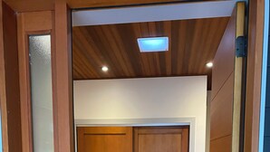 Puerta de madera con felpudo texturizado en la entrada, techo con iluminación empotrada y vista a una habitación con suelo de madera.