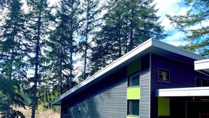 Una casa moderna de dos pisos con balcón, rodeada de árboles altos.