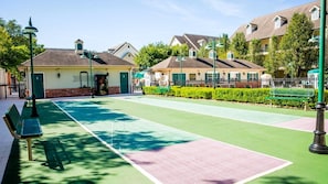 Een tennisbaan met banken, een hek en huizen op de achtergrond.