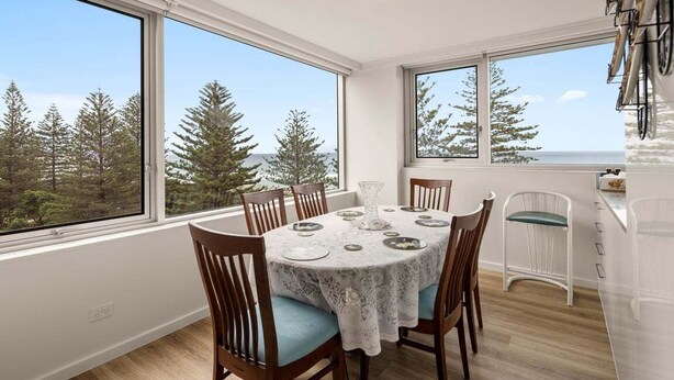 A dining area with a table set for four, large windows, and a view of trees. - Coastal Comfort with Ocean Views | Oceania 19 (Gold Coast)