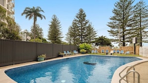 A swimming pool with lounge chairs, surrounded by trees and a fence. - Coastal Comfort with Ocean Views | Oceania 19 (Gold Coast)