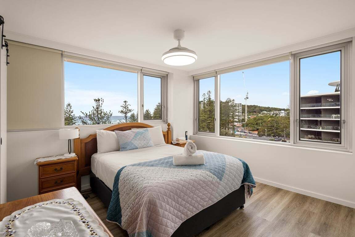 Una camera da letto con un letto, comodini, una lampada e ampie finestre con vista.