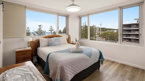 A bedroom with a bed, bedside tables, a lamp, and large windows with a view. - Coastal Comfort with Ocean Views | Oceania 19 (Gold Coast)