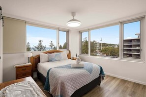 Un dormitorio con cama, mesitas de noche, lámpara y ventanas grandes con vistas.