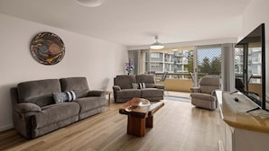 A modern living room with a sofa set, a coffee table, and a dining area with a wooden table. - Coastal Comfort with Ocean Views | Oceania 19 (Gold Coast)