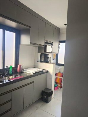 Uma cozinha moderna com armários cinzentos, micro-ondas, máquina de café e lixeira.