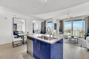 Un appartement moderne doté d’un îlot de cuisine, d’un coin repas et d’un espace de vie avec de grandes fenêtres offrant une vue sur la ville.
