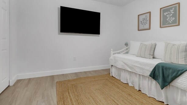 Un dormitorio con cama, televisor montado en la pared y una mesita de noche.