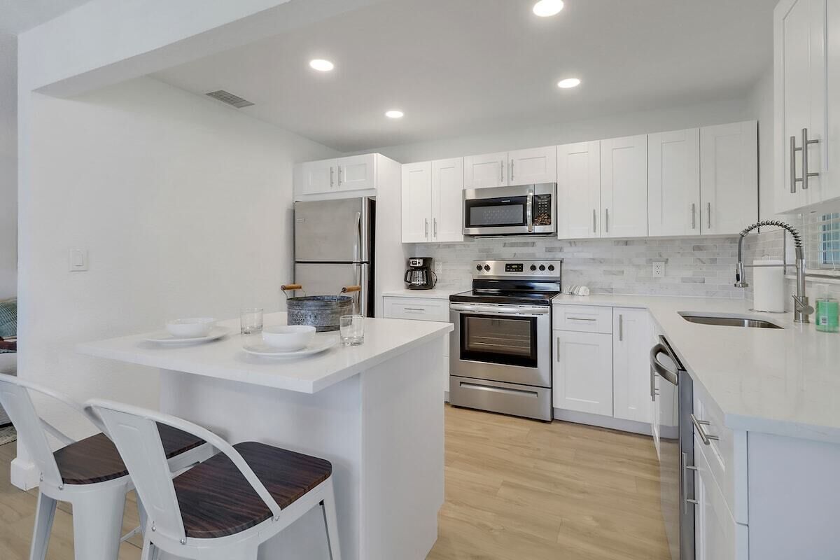 A modern kitchen with white cabinetry, stainless steel appliances, and a central island with seating.