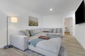 A modern living room with a sectional sofa, a floor lamp, a painting, and a flat-screen TV. - Bayshore Bungalow- Located near Beaches & Downtown (Naples)