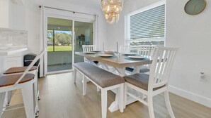 Un comedor con una mesa dispuesta para cuatro, sillas blancas y una araña.