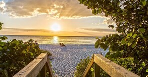 Eine Holzterrasse, die zu einem Strand mit Sonnenuntergang führt.