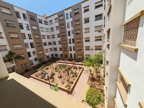 Un edificio residencial de varios pisos con balcones, un patio central con plantas y un cielo despejado.
