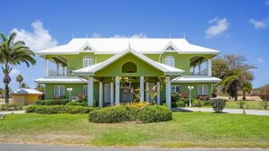 A large, two-story house with a symmetrical facade, a central entrance, and a covered porch. - Spacious 5-bedroom villa in beautiful Lowlands with AC (Lowlands)
