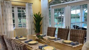A dining area with a table set for four, surrounded by wicker chairs, with a view of the outdoors through large windows. - Spacious 5-bedroom villa in beautiful Lowlands with AC (Lowlands)