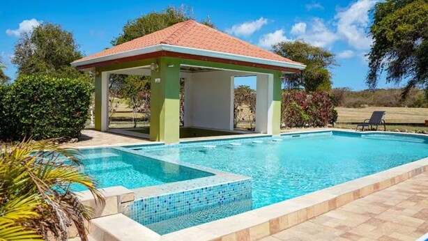 A swimming pool with a covered pavilion, surrounded by greenery and a clear sky. - Spacious 5-bedroom villa in beautiful Lowlands with AC (Lowlands)