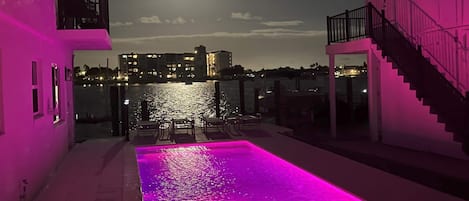 A pool with pink lighting, a staircase, and a view of the city at night.