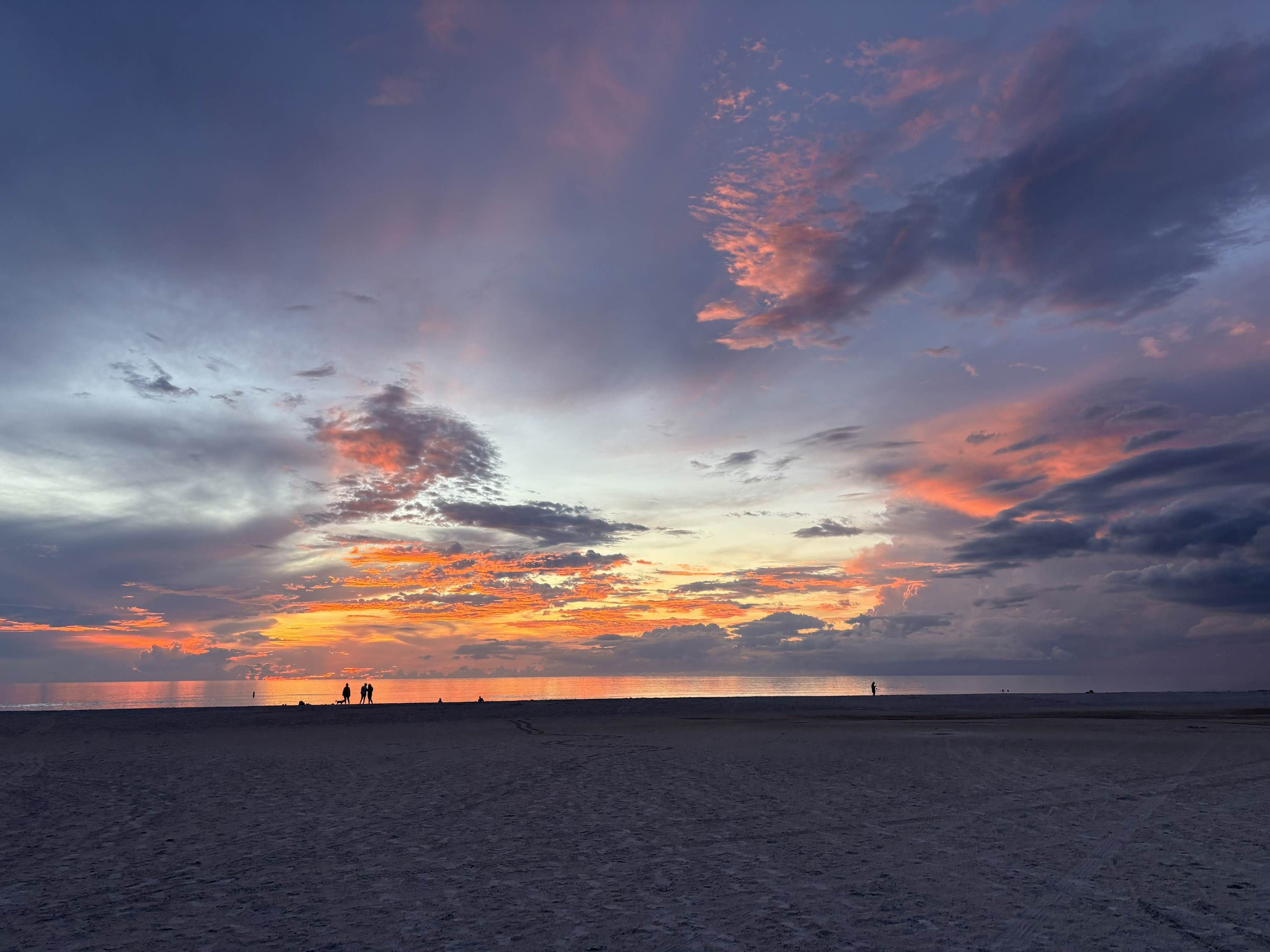 Une plage au coucher du soleil, avec des silhouettes de personnes.