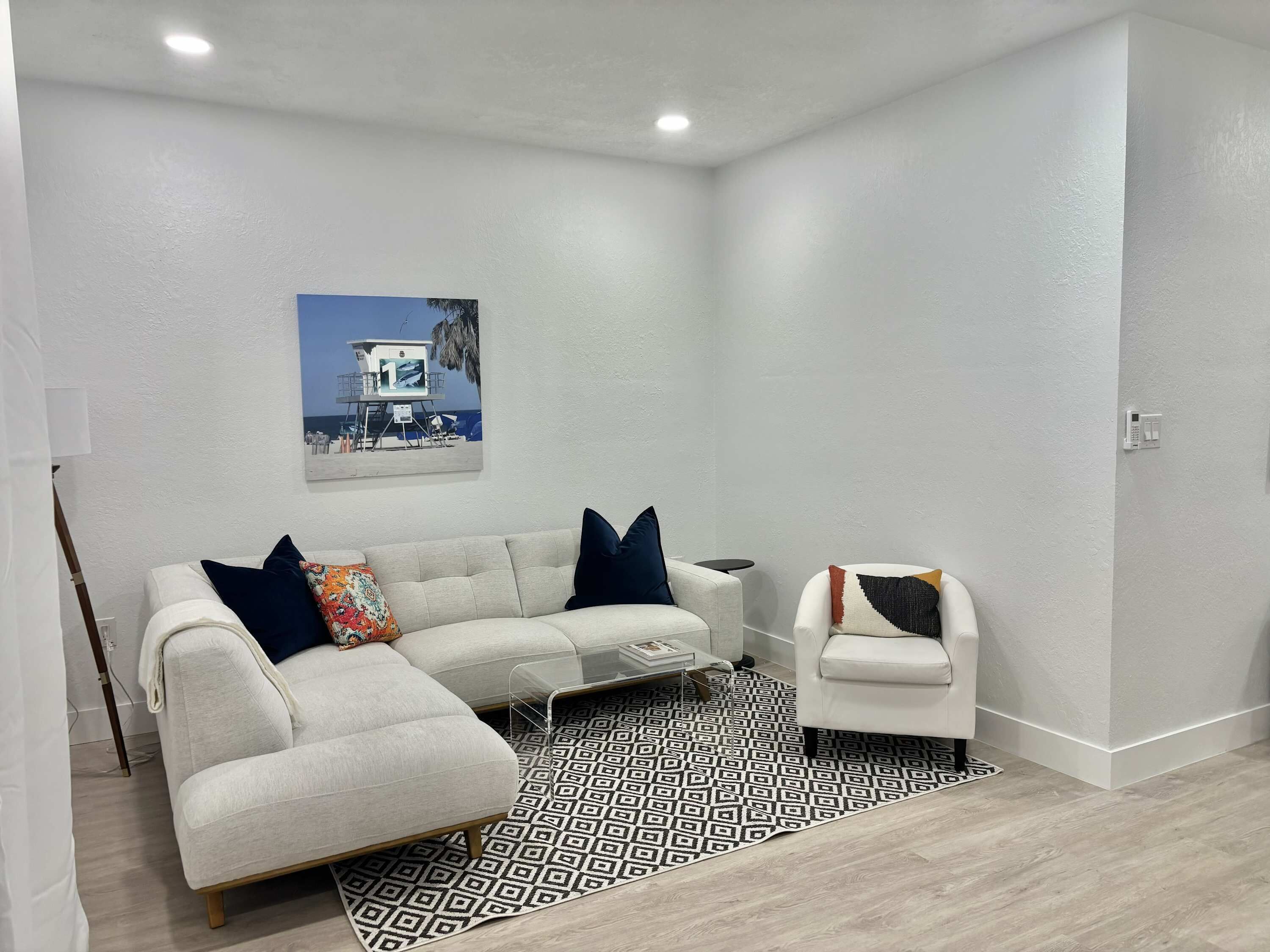Una sala de estar moderna con un sofá, un sillón, un tapete estampado y un cuadro con una escena de playa.