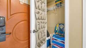 Una habitación con una puerta, un mueble de almacenamiento en la pared, una cama con una colcha colorida y una estantería con objetos.