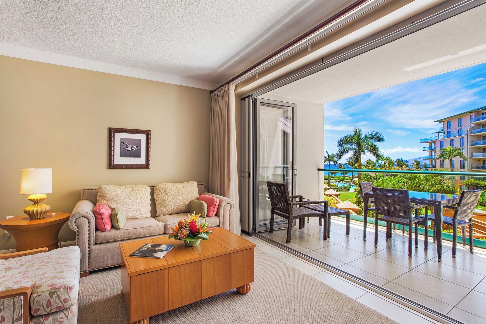 A hotel room with a sofa, coffee table, and a balcony with outdoor furniture.
