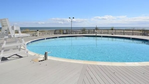 En pool med ett trädäck, ett metallräcke och fri utsikt över havet.